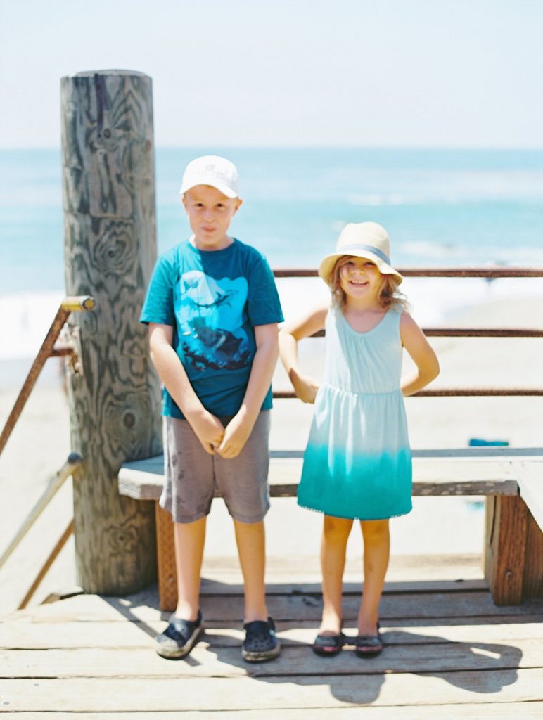 A brother and sister smile in front of the surf during their Malibu kids photo session with portrait photographer Daniele Rose