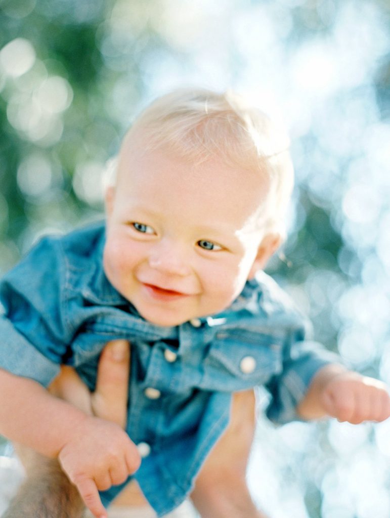 A baby boy smiles while being lifted into the air during a family portrait session