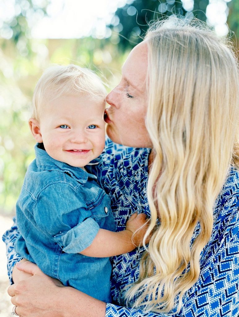 A baby smiles while his mother kisses him on the head during their Camarillo holiday mini session