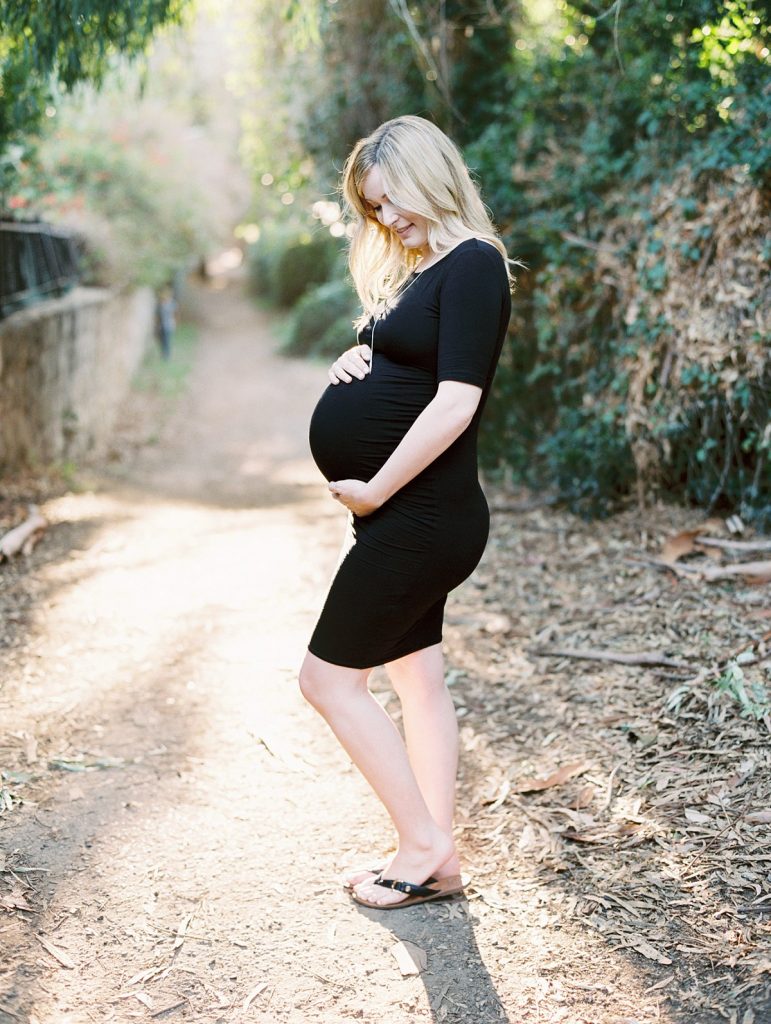 A pregnant woman in a black dress looks down at her belly in Santa Barbara