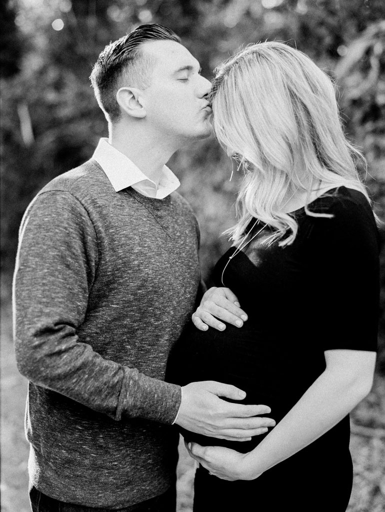Black and white image of a new dad kissing his pregnant wife on the forehead