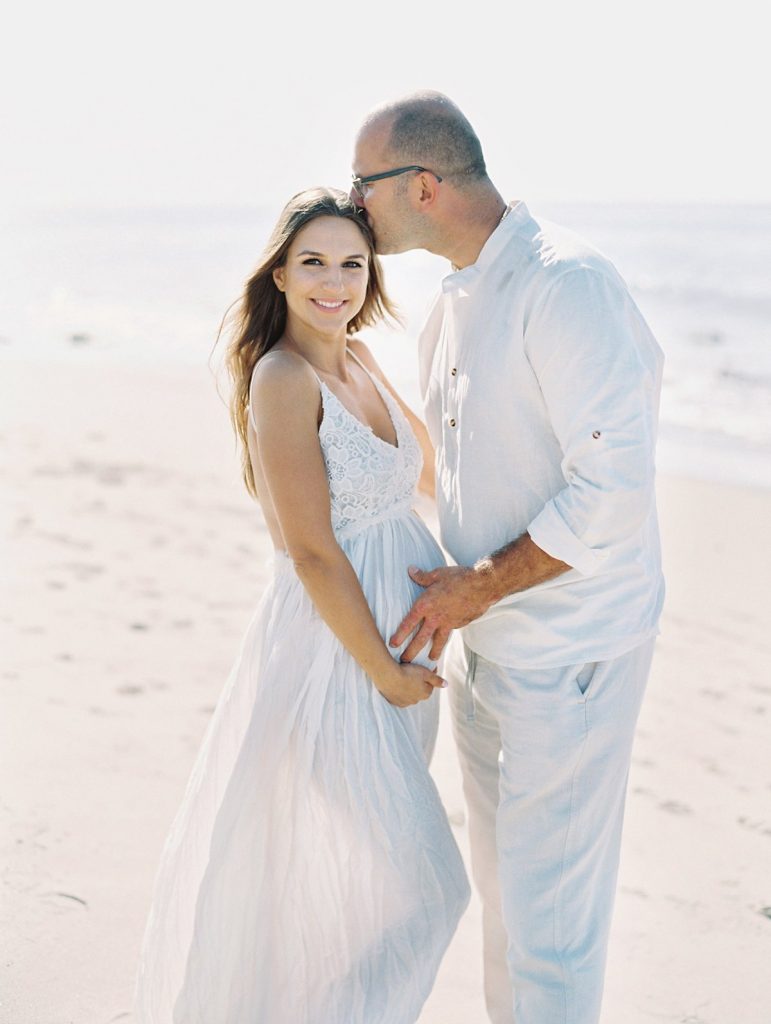 A man kisses his pregnant wife on the forehead during their Santa Barbara beach maternity portraits