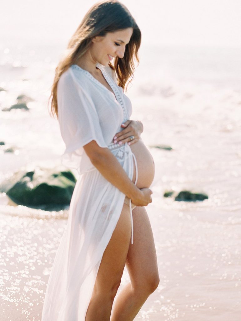 A maternity portrait of a woman wearing a white dress on the beach in Santa Barbara, California