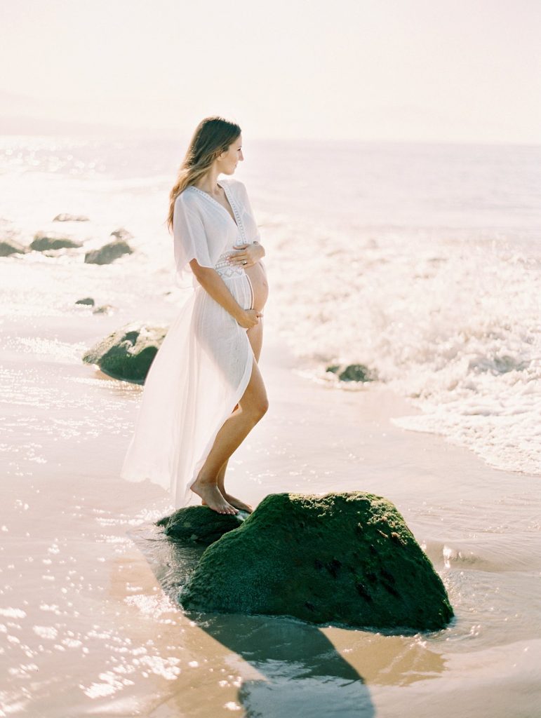 A maternity portrait of a woman standing on moss covered rocks in the surf at Hammond's Beach in Santa Barbara