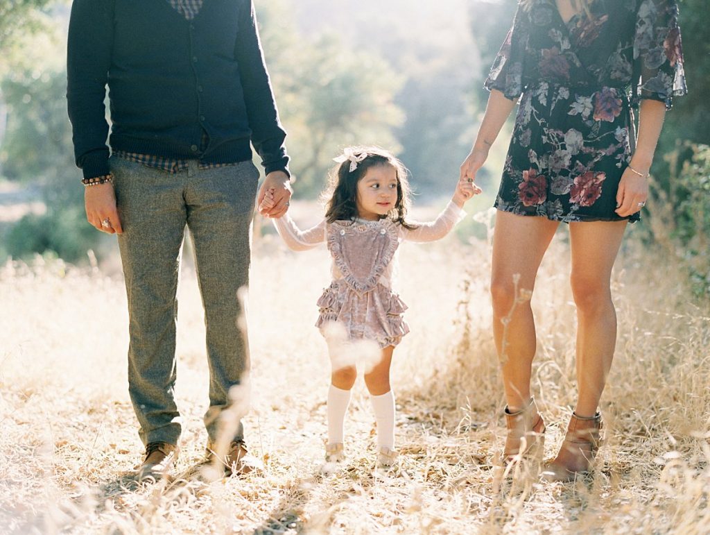 Photo of parents holding their young daughter's hands in a field of golden grass in Thousand Oaks, California