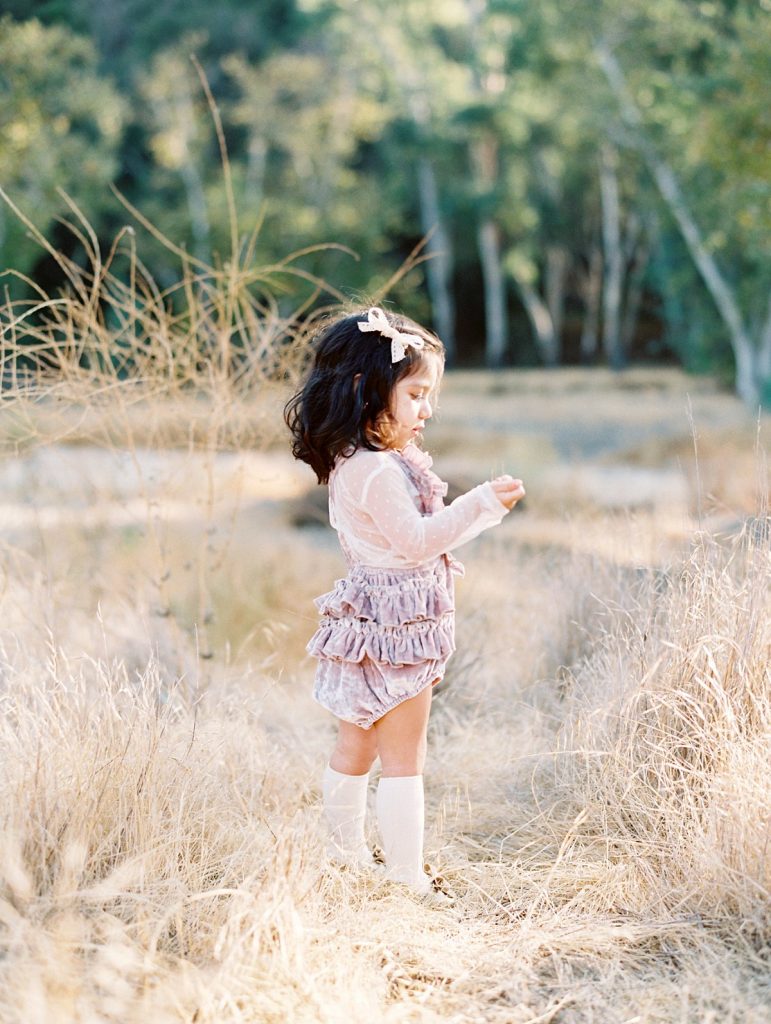 A young girl wearing ruffled bloomers stands in a field of yellow grass in Thousand Oaks