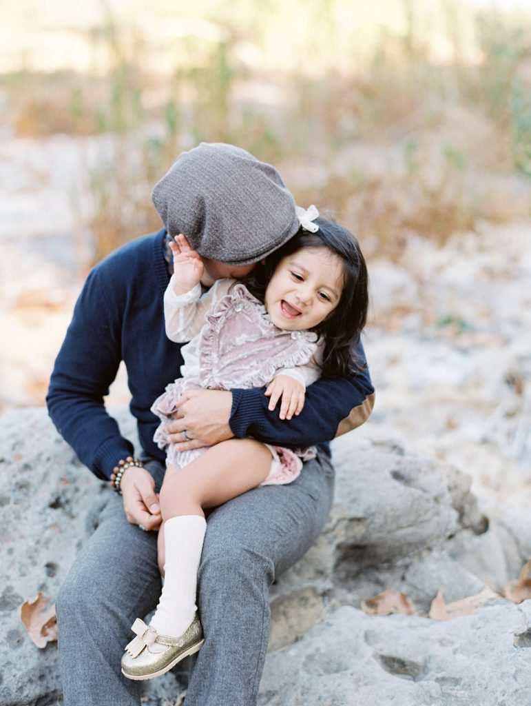 A father holds his daughter on his lab during a family portrait session at Peter Strauss Ranch in Thousand Oaks