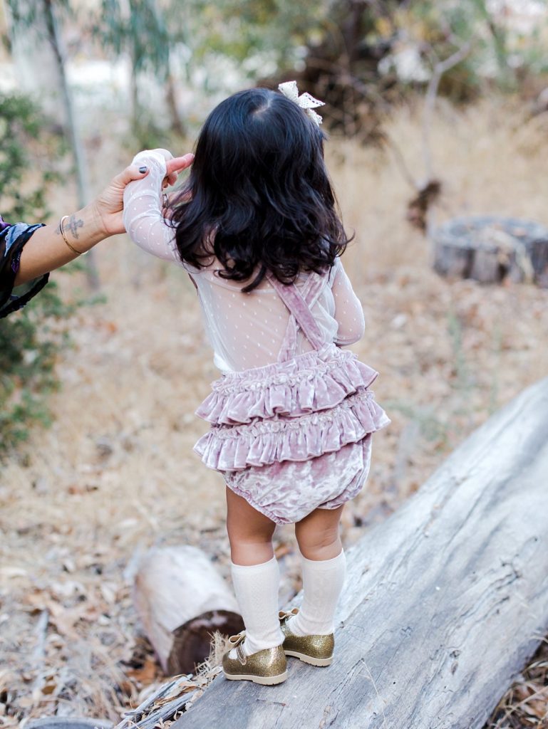 A little girl with ruffled bloomers walks on a long at Peter Strauss Ranch