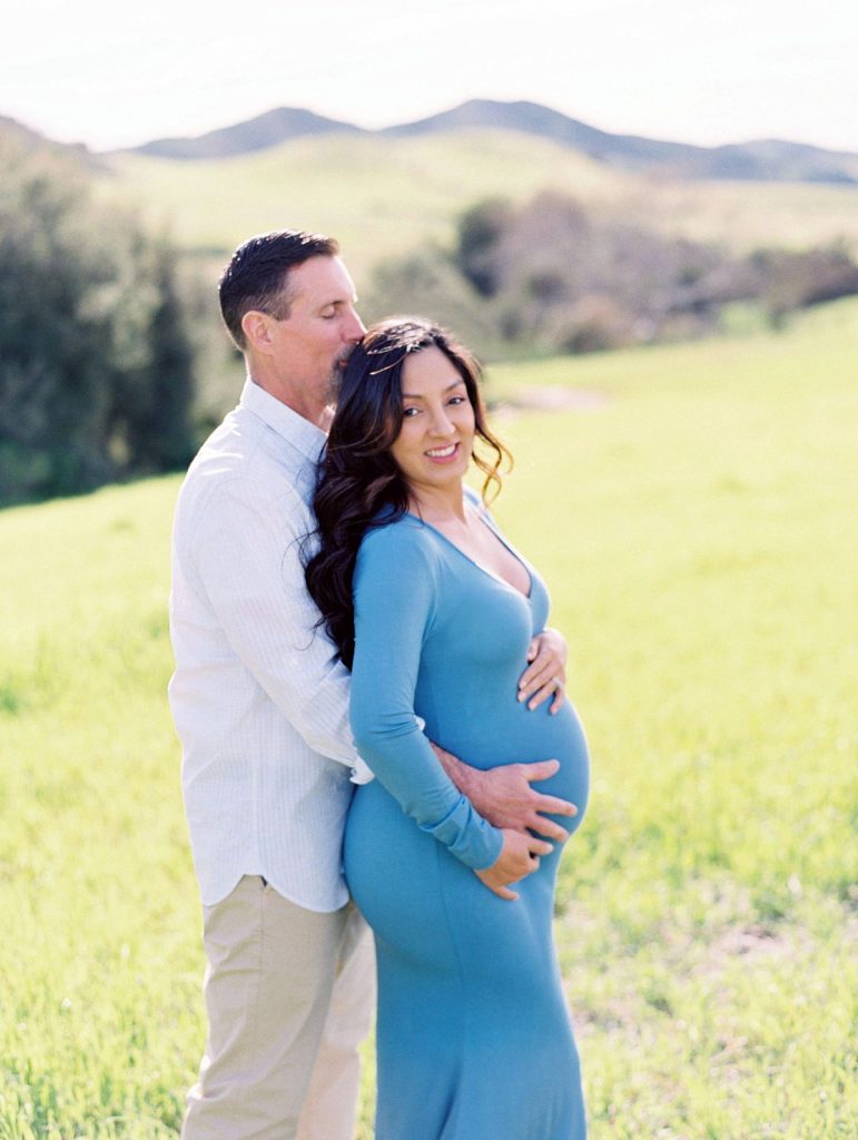 A husband touches his wife's pregnant belly during their maternity portrait session in a field in Thousand Oaks