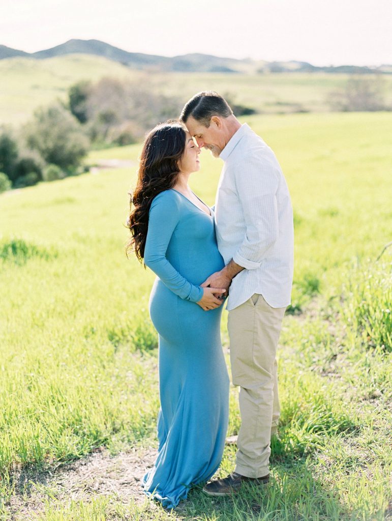 A couple embraces in a green field during their maternity session in Thousand Oaks, California