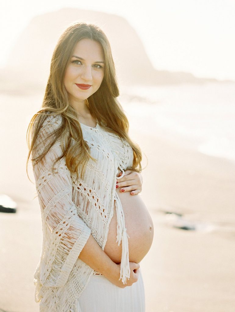 A beach maternity portrait of an expecting mother smiling at the camera