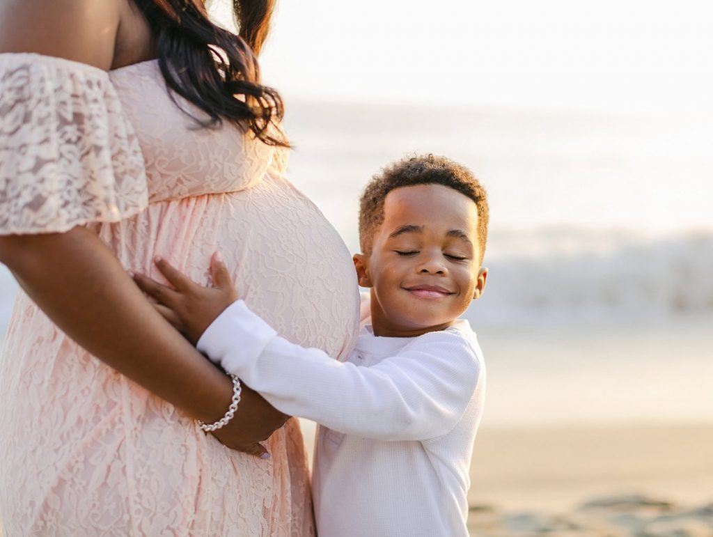 A young boy hugging his mother's pregnant belly in a post about what to wear for a maternity photo session.