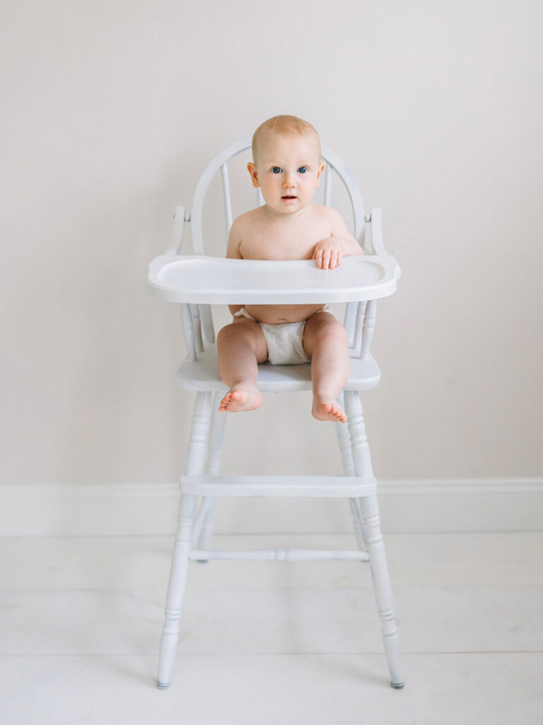 A six month old baby sitting in a vintage white high chair during his six month sitter session with Camarillo photographer Daniele Rose.