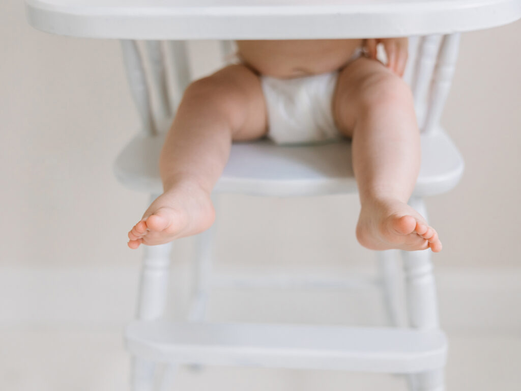 A close up photos of a baby's toes while he is sitting in a white vintage high chair during his six month sitter session with Camarillo photographer Daniele Rose.