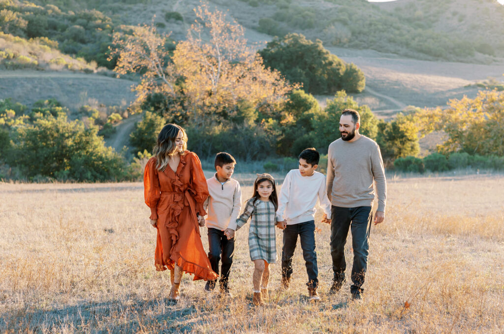 A family dressed in fall colors strolls through a field with golden trees in the background.