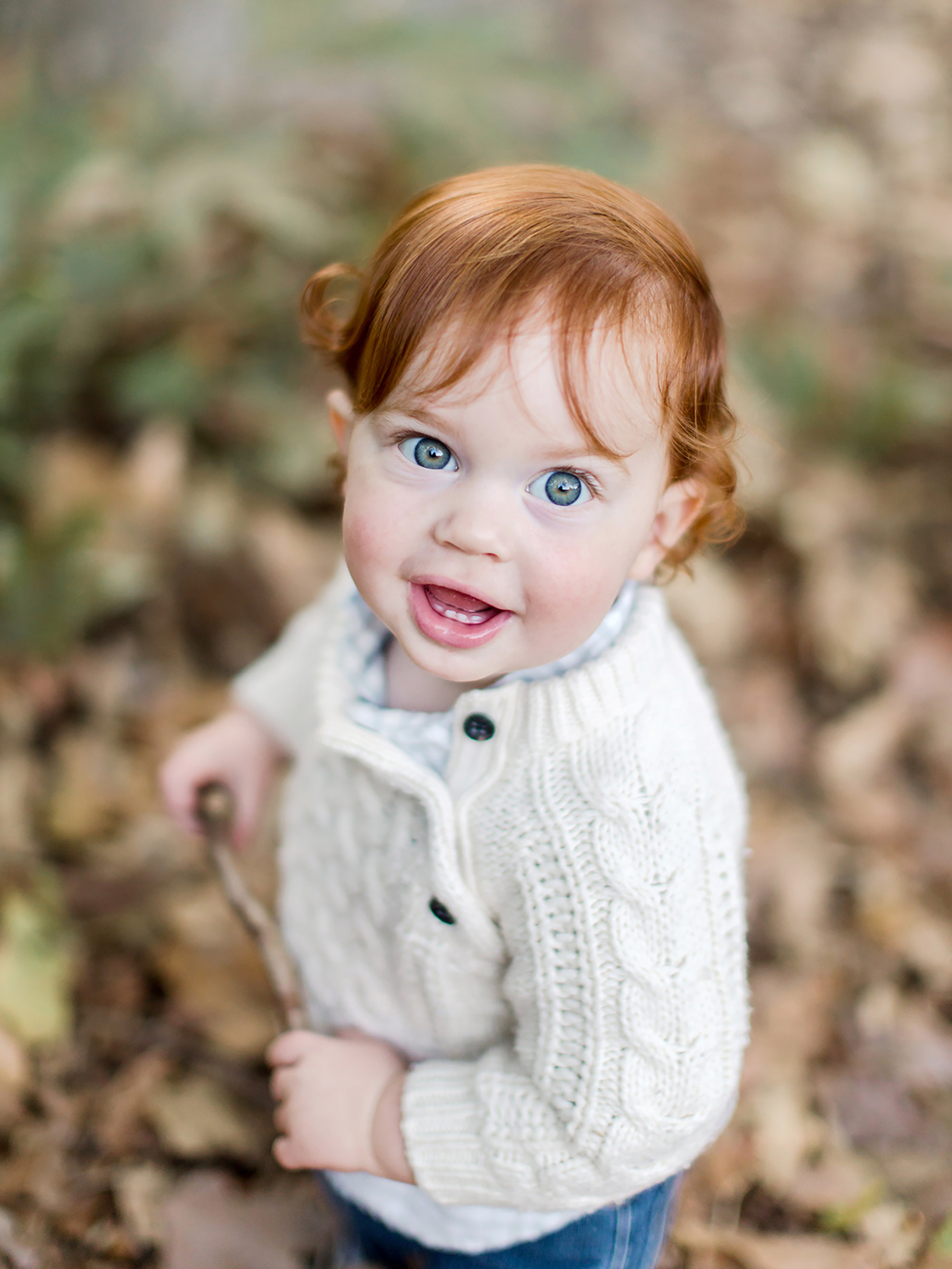 A toddler with red hair and blue eyes plays in the leaves during a photo session and is the perfect example of fall family photo outfit ideas.