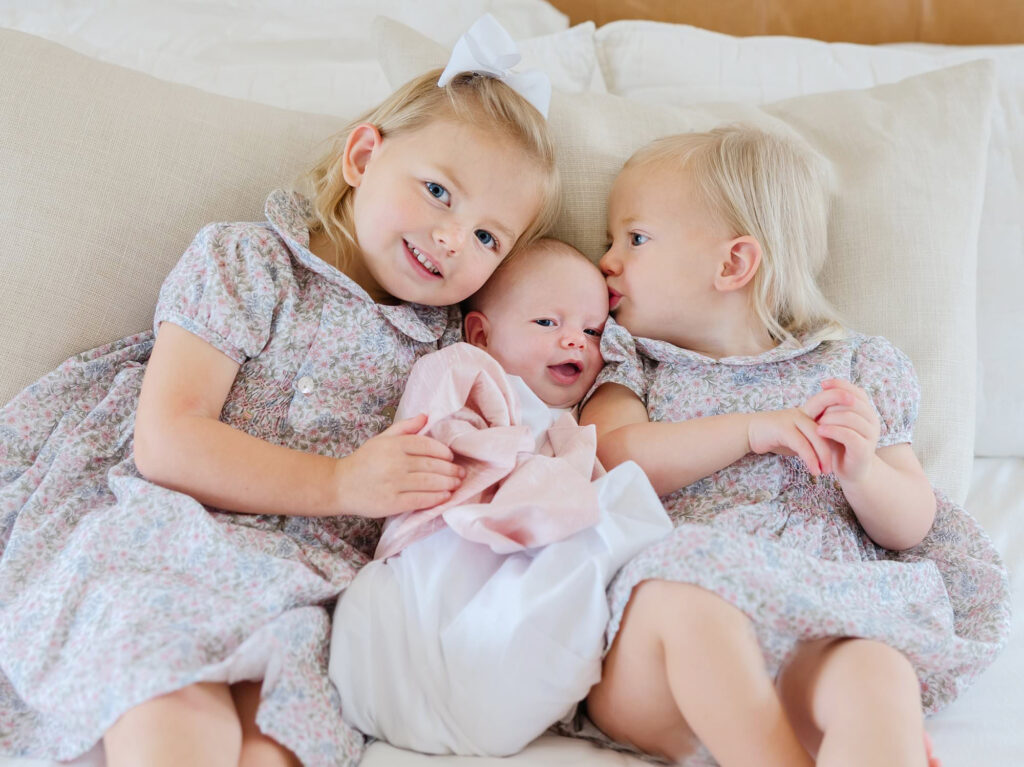 Three sisters snuggle in their parents bed during a photo session.