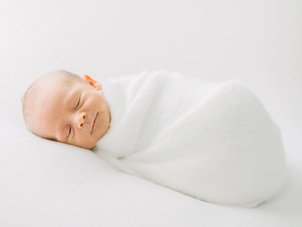 A baby in a white swaddle smiles during a studio photography session.