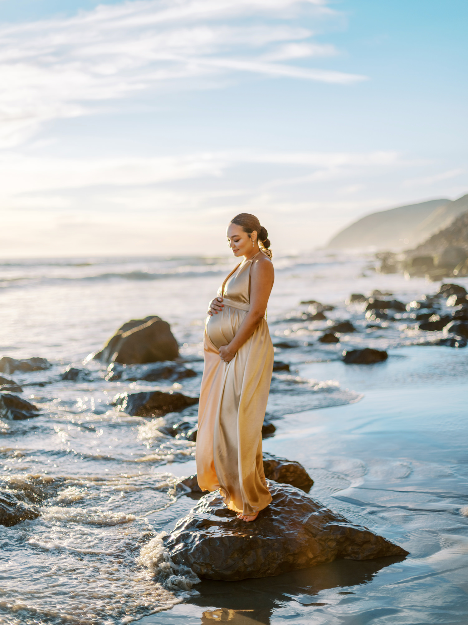 Maternity photographer Los Angeles Daniele Rose captures an image of a mother to be wearing a gold dress on the beach in Malibu