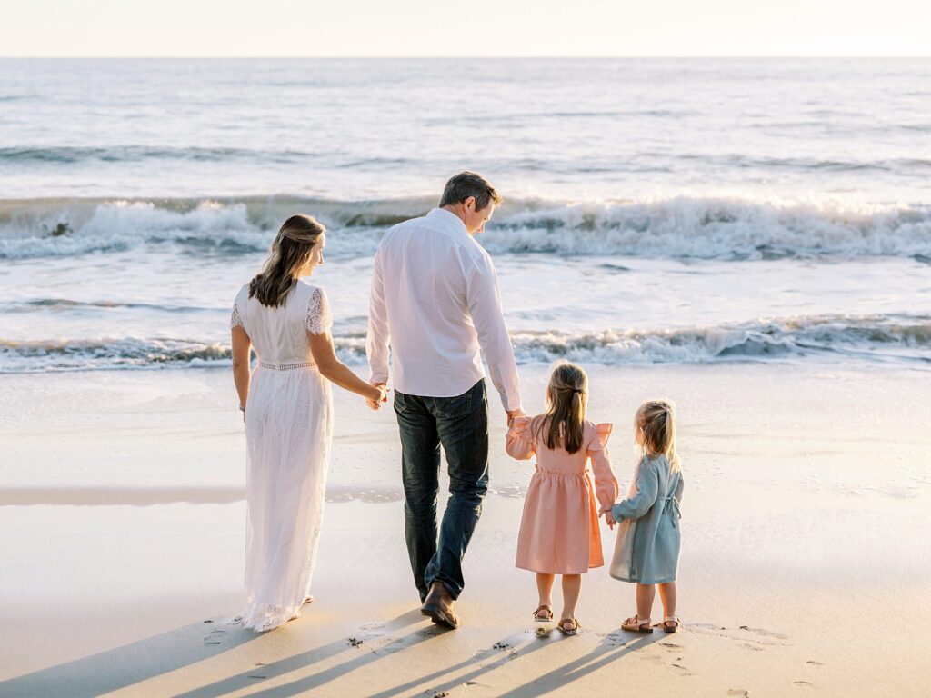 Family walking on beach in coordinated summer family photo outfits with flowing dresses and casual shirts