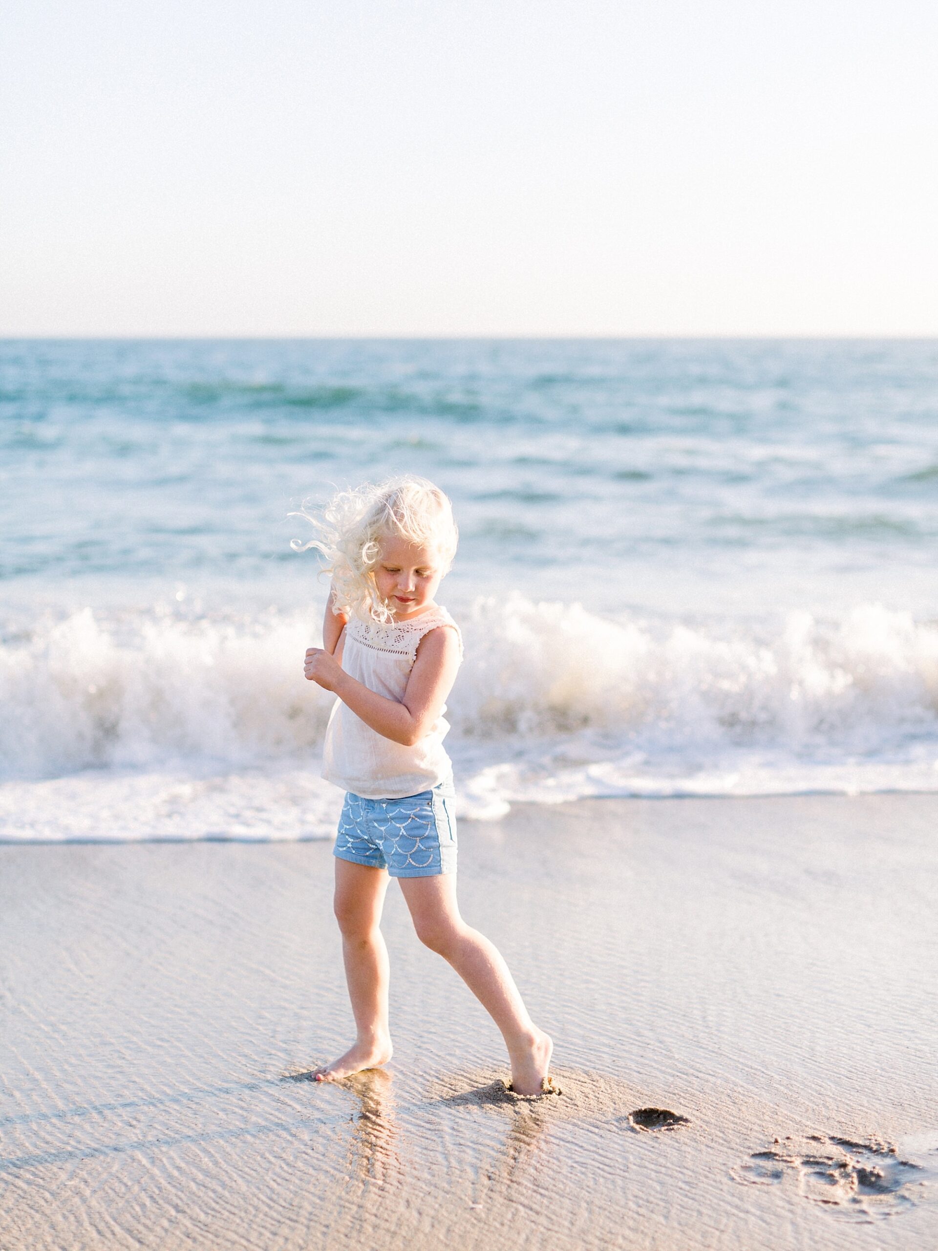 Young girl in light blue dress running on beach during golden hour photography session