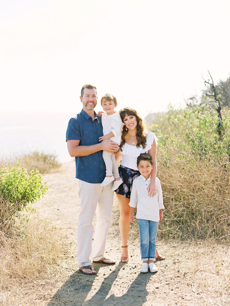 Happy family of four photographed by Malibu family photographer on scenic coastal trail during golden hour
