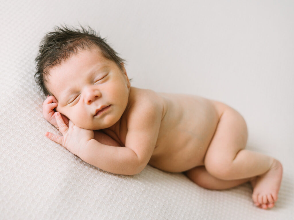 Must-have newborn photos include baby alone sleeping peacefully in classic curled pose on cream textured blanket
