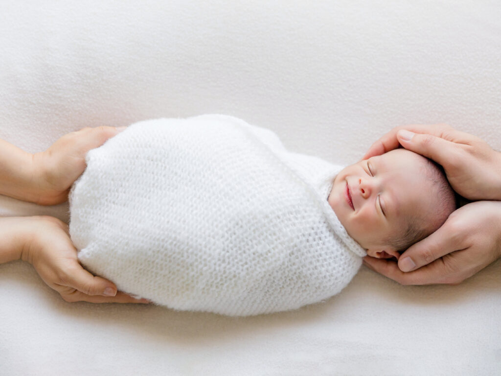 Parents' hands gently holding wrapped newborn baby demonstrating scale in professional photography session
