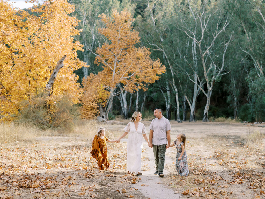 Parents walking hand in hand with their children through the fall leaves during their Southern California golden hour fall family photos.
