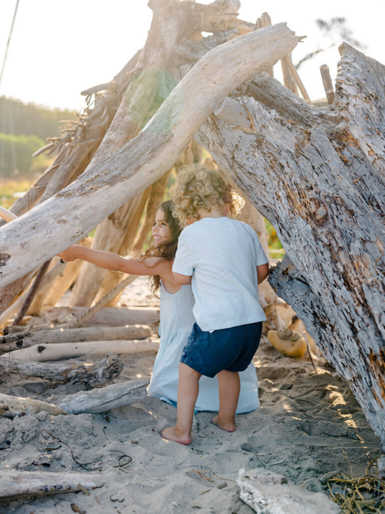 Young siblings playing together among driftwood during candid family photos