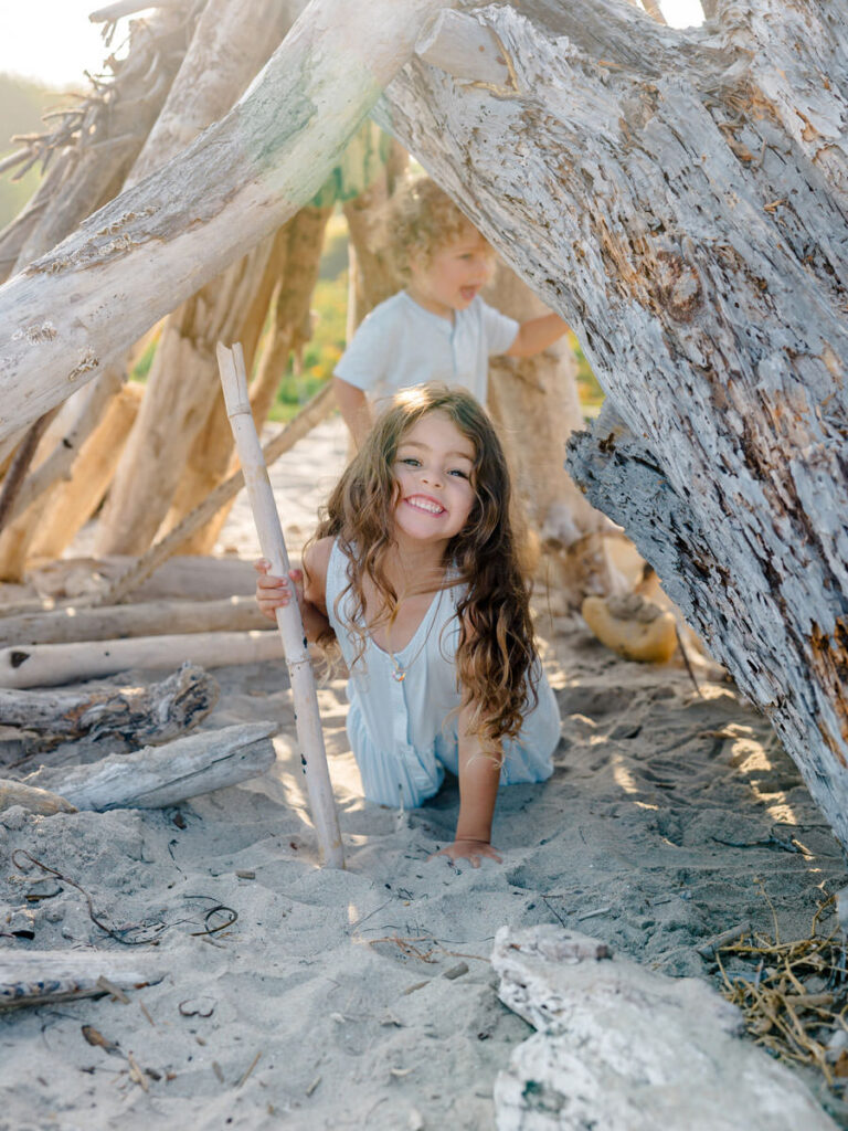 Smiling young girl playing in a driftwood fort during a family beach session
