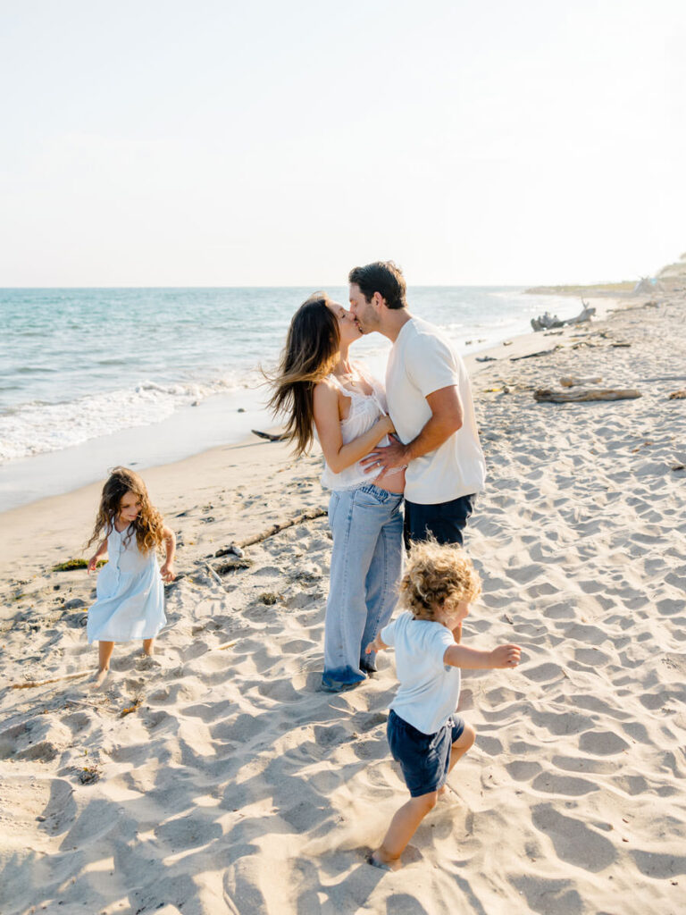 Parents kissing while their kids run and play during a candid Santa Barbara family photography session