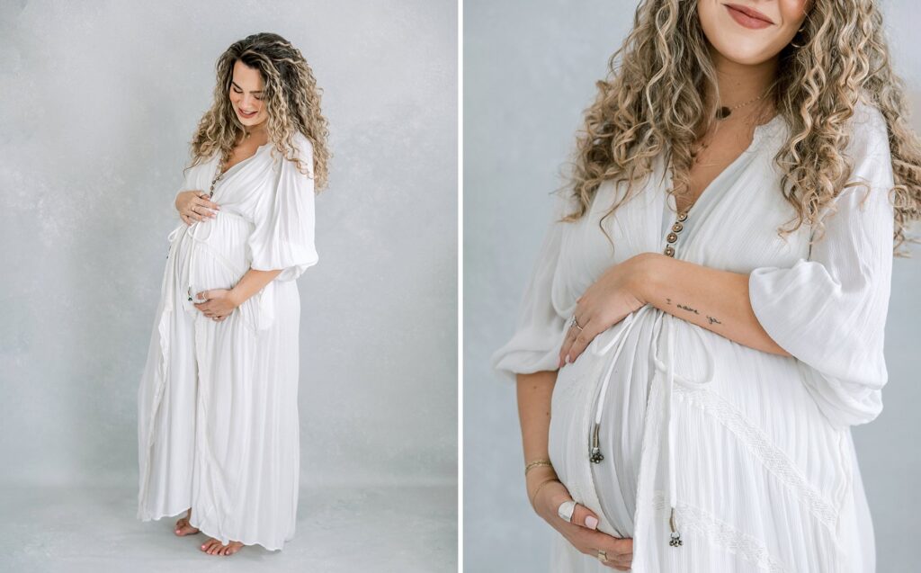 Expecting mother in a white dress holding her belly in the natural light studio of Daniele Rose Photography