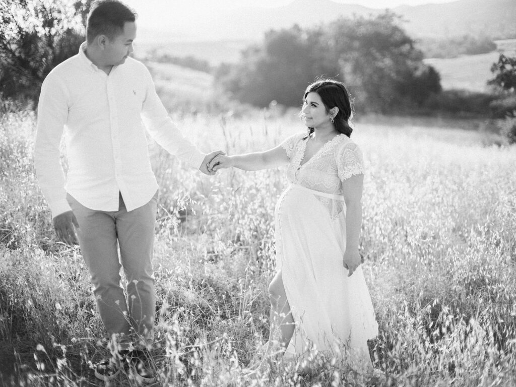 Expecting couple holding hands and walking together through a sunlit field
