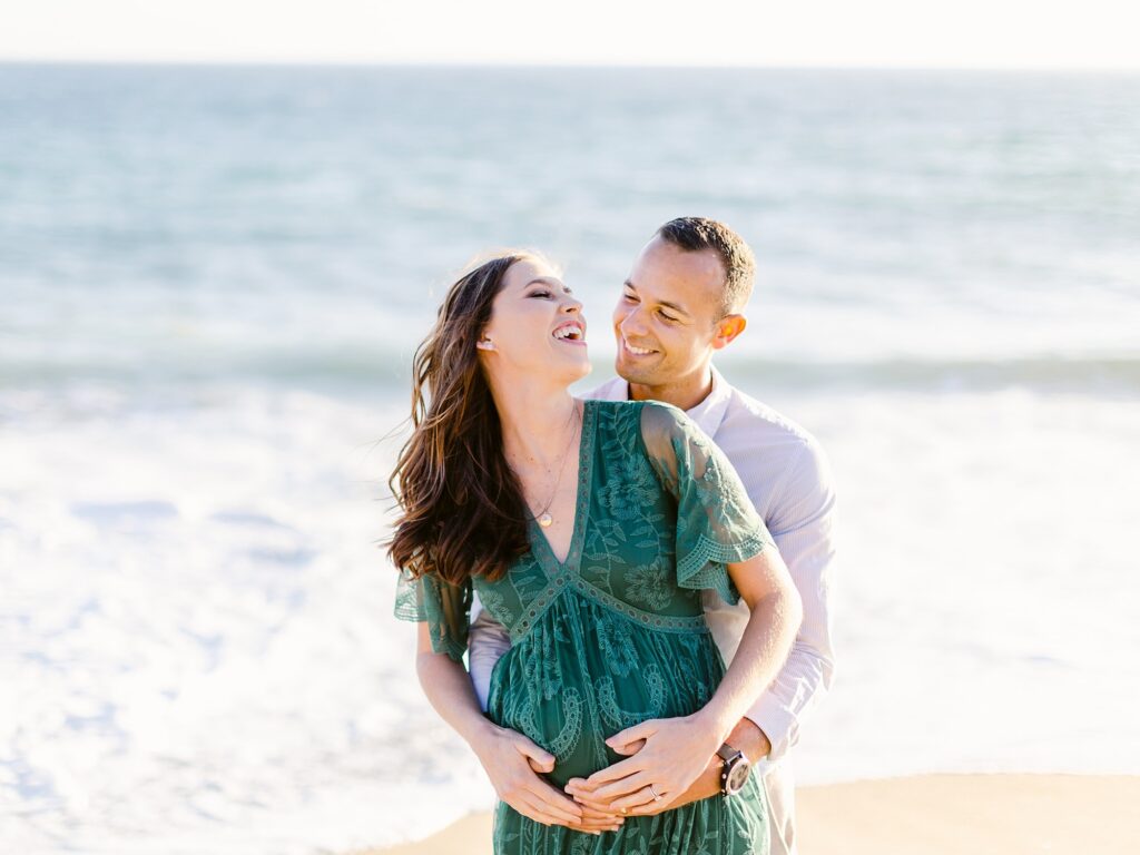 When to take maternity photos of an expecting couple embracing with the ocean behind them