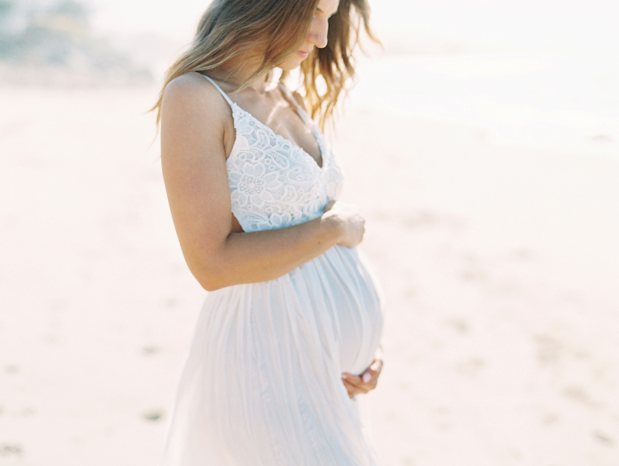 When to take maternity photos of an expecting mother posing on the beach in a white dress